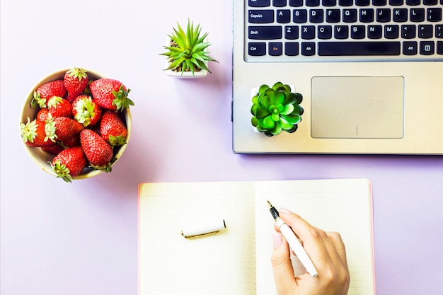 Lugar de trabajo acogedor de primavera con una computadora portátil, un cuaderno, un tazón de fresas