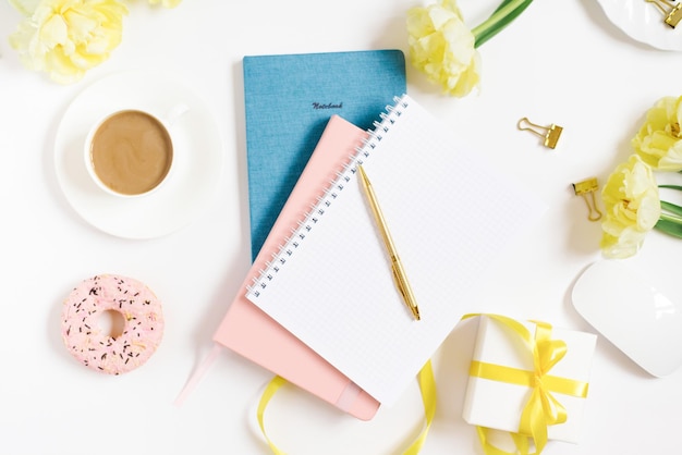 Lugar de trabajo de una bloguera o freelance Varios cuadernos un bolígrafo dorado una taza de café con donas una caja de regalo de cumpleaños flores Pausa para el café