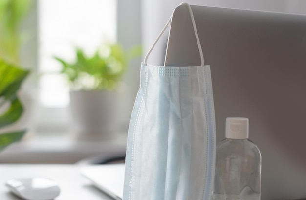 Lugar de trabajo en casa junto a la ventana con una mascarilla protectora para computadora portátil y concepto de desinfección de cuarentena durante la pandemia de coronavirus en el mundo