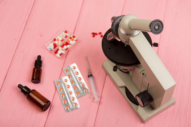 Lugar de trabajo científico médico microscopio píldoras jeringa en mesa de madera rosa