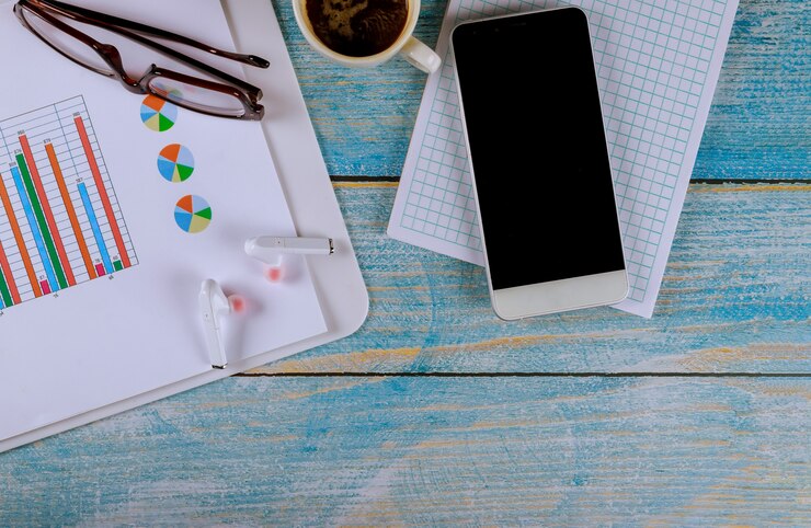 Foto lugar de trabajo comercial con gadgets para teléfonos inteligentes y auriculares inalámbricos y café, gafas con gráficos y diagramas