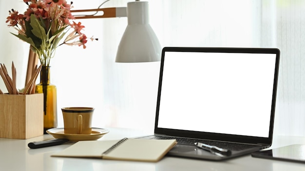 Lugar de trabajo cómodo con lámpara de computadora portátil y taza de café en la mesa blanca