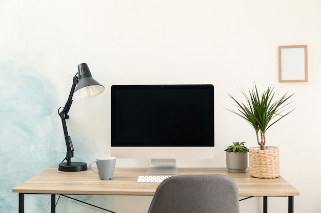 Lugar de trabajo con computadora y planta en mesa de madera. Azul claro y blanco