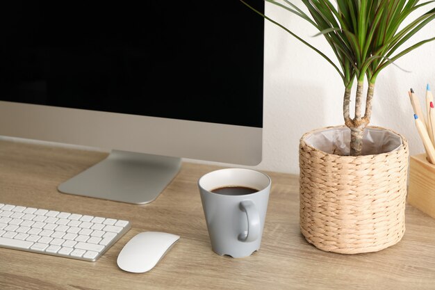 Lugar de trabajo con computadora, planta y taza de café en la mesa de madera, de cerca