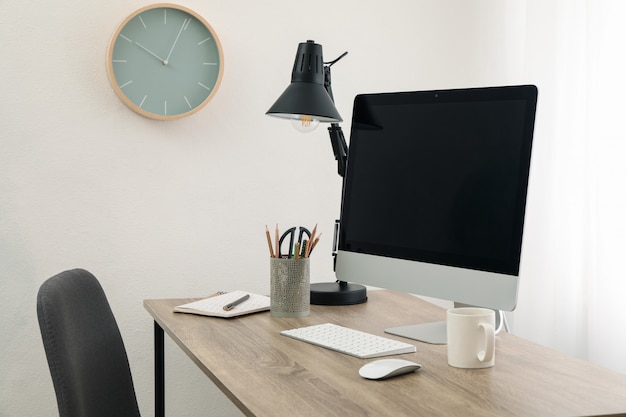 Lugar de trabajo con computadora, taza y lámpara de mesa de madera. Blanco