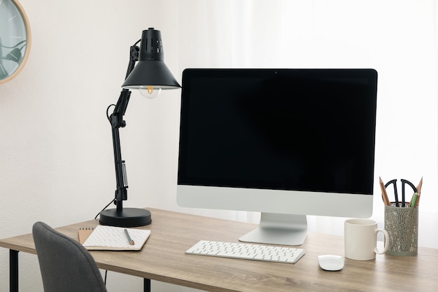 Lugar de trabajo con computadora, taza y lámpara de mesa de madera. Blanco