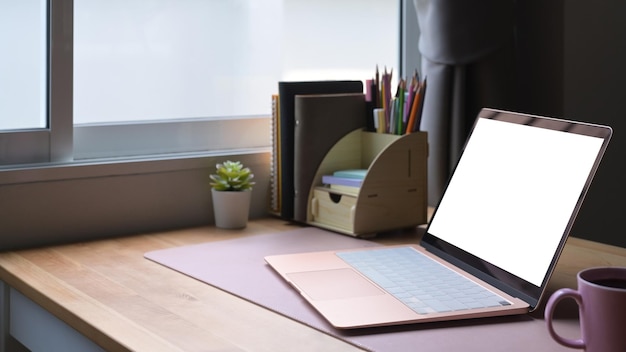 Lugar de trabajo contemporáneo con taza de café de computadora portátil y suministros en mesa de madera