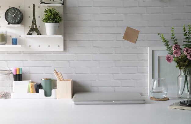 Lugar de trabajo creativo con maceta de marco de imagen portátil y papelería en mesa blanca