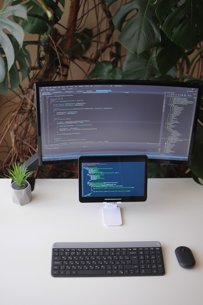 Foto lugar de trabajo para desarrollador, pantalla y tableta con código. confort trabajando desde casa con plantas