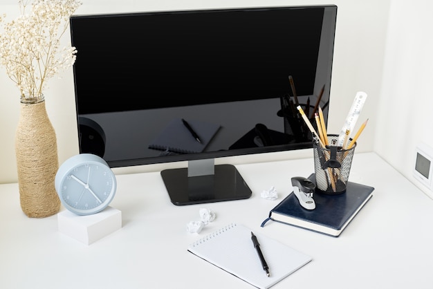 Lugar de trabajo con escritorio, reloj, suministros de oficina y rama de flores en un jarrón