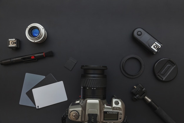 Lugar de trabajo de fotógrafo con lente y accesorio de cámara sobre fondo de mesa negro oscuro