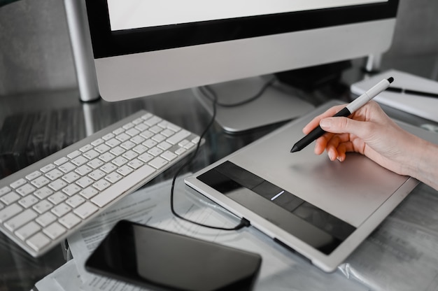 Lugar de trabajo de fotógrafo o diseñador gráfico. Manos creativas del diseñador que trabajan en la computadora portátil con la tableta gráfica. Monitor de computadora, teclado, cuaderno vacío, mouse, teléfono inteligente