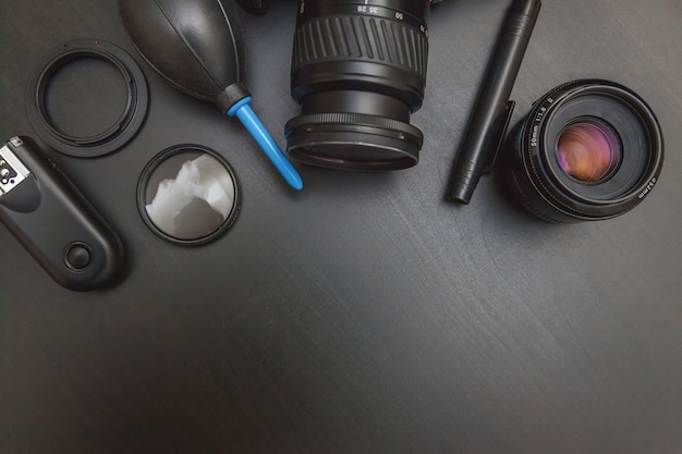 Lugar de trabajo del fotógrafo con sistema de cámara réflex digital, kit de limpieza de cámara, lente y accesorio de cámara sobre fondo de mesa negro oscuro