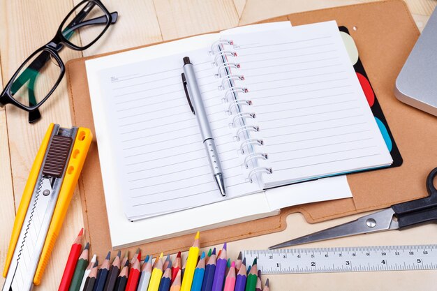 Lugar de trabajo con lápices de colores y suministros portátil anteojos en mesa de madera