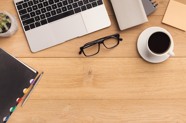 Lugar de trabajo masculino con laptop, taza de café, cuaderno y vasos. Fondo de madera, vista superior, maqueta, espacio de copia.