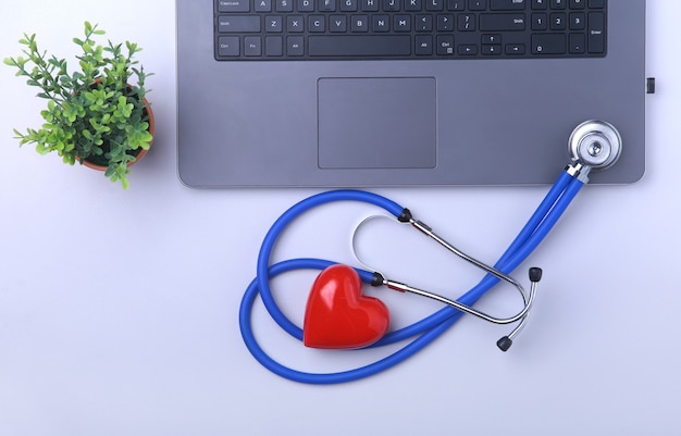 Foto lugar de trabajo de médico con laptop, estetoscopio, prescripción de rx, gafas y corazón rojo y cuaderno sobre mesa blanca. vista superior. copie el espacio.