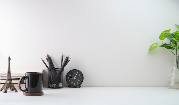 Lugar de trabajo mínimo con libros, taza de café y portalápices en mesa blanca Copie espacio para su texto