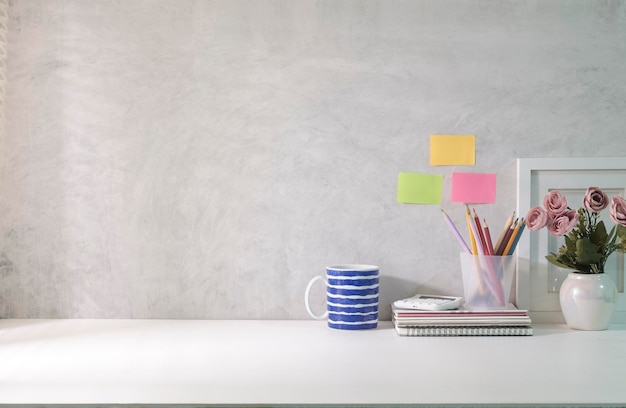 Lugar de trabajo mínimo con un marco de imagen vacío, una taza de café y un portalápices en una mesa blanca. Copie el espacio para su texto.