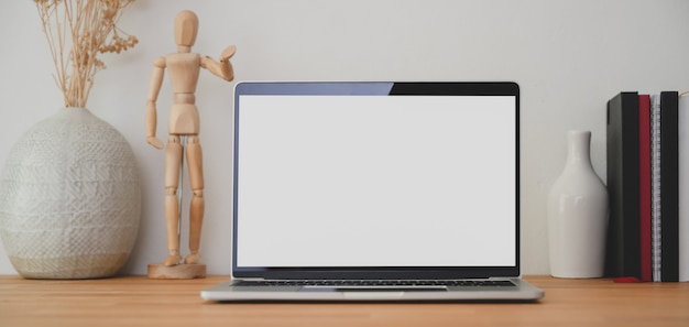 Lugar de trabajo moderno con computadora portátil de pantalla en blanco y suministros de oficina en mesa de madera