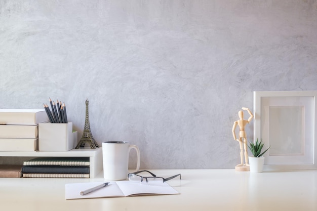 Lugar de trabajo moderno y luminoso con marco de fotos de taza de café de maceta y libros en mesa blanca Copie espacio para su texto