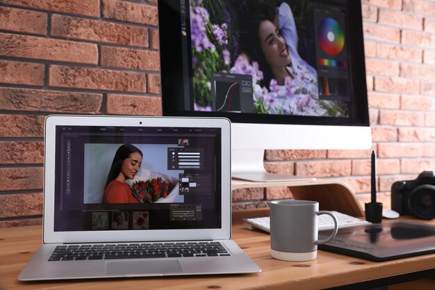 Lugar de trabajo moderno del retocador con diferentes dispositivos digitales en la mesa de madera cerca de la pared de ladrillo rojo