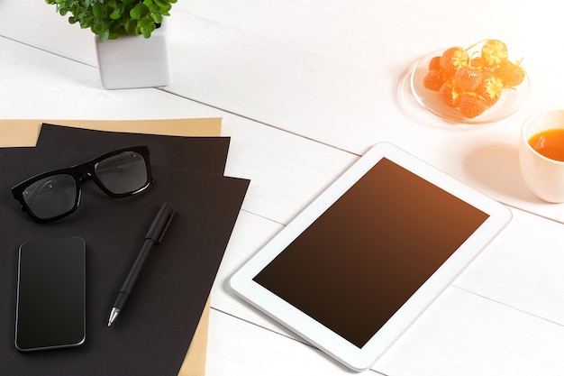 Lugar de trabajo moderno con tableta digital y teléfono móvil, taza de café, bolígrafo y hoja de papel vacía. Vista superior y espacio para copiar texto.