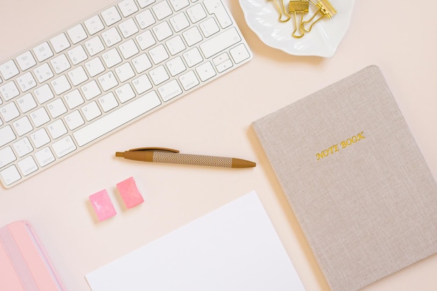 El lugar de trabajo de una mujer con un cuaderno beige, un teclado de computadora y un bolígrafo Vista superior plana