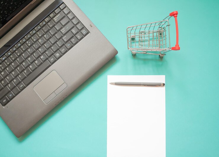 Foto lugar de trabajo en la oficina en casa con gadgets, papelería, teclado de computadora, carrito de supermercado, compras en línea