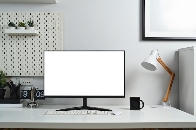 Lugar de trabajo de oficina en el hogar con pantalla de computadora en blanco taza de café y papelería contra pared blanca