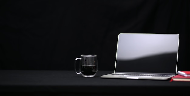 Lugar de trabajo oscuro y moderno con computadora portátil abierta, taza de café y cuaderno