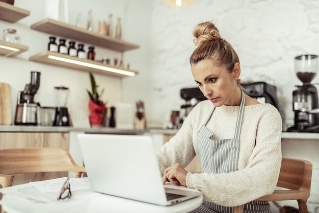 Lugar de trabajo. Propietario de café inteligente enfocado sentado en la mesa trabajando en su computadora portátil.