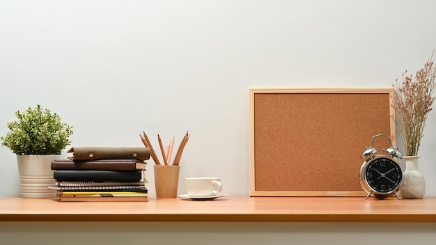 Lugar de trabajo simple con libros de alarma de tablero de polla en blanco y planta en maceta en la mesa de madera