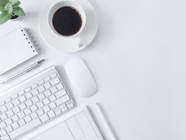 Lugar de trabajo con taza de café, cuaderno, planta de plástico y teclado.