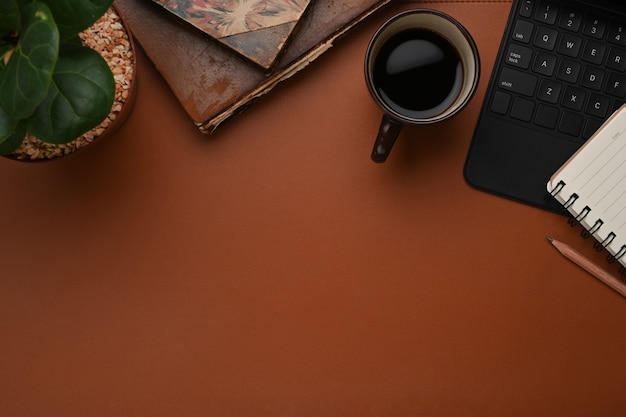 Foto lugar de trabajo con taza de café, cuaderno, teclado y espacio de copia de cuero marrón.