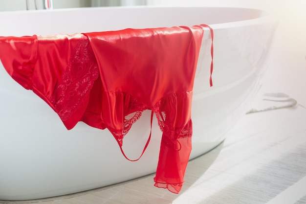 Lujoso camisón de satén y bata en rojo colgados en la bañera del baño