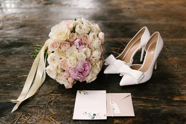 Un lujoso ramo de novia con rosas blancas junto a zapatos e invitaciones de boda sobre un fondo de madera