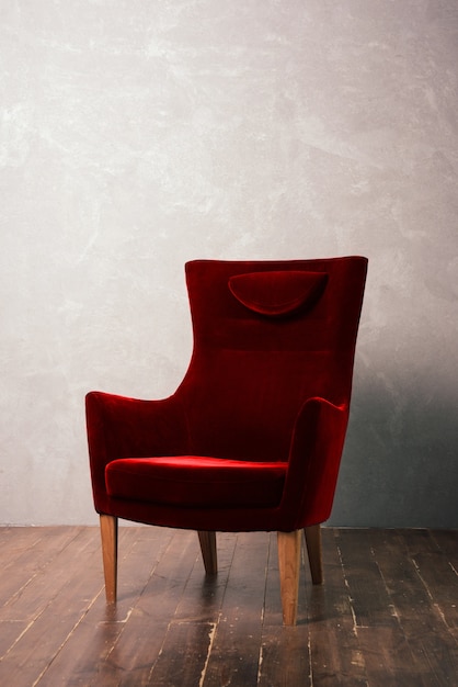 Lujoso sillón de terciopelo rojo se encuentra cerca de la pared de textura en un piso de madera oscura.