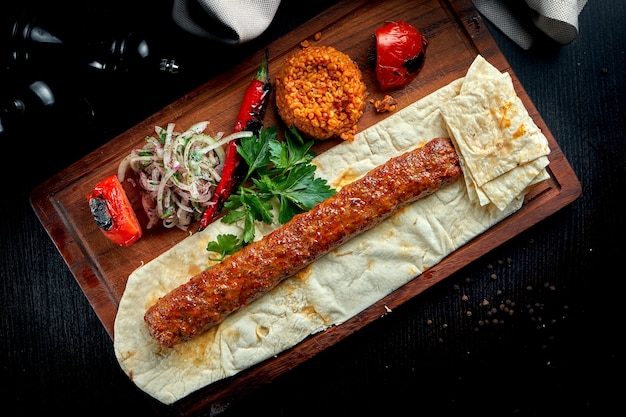 Lula kebab de cordero turco a la parrilla con verduras asadas, cebolla y arroz sobre tabla de madera