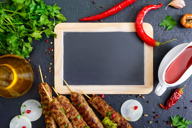 Lula Kebab ist ein traditionelles arabisches Gericht. Fleischschaschlik auf Holzspießen, würzige Tomatensauce auf schwarzem Hintergrund. Freier Platz zum Schreiben auf die Tafel in der Mitte