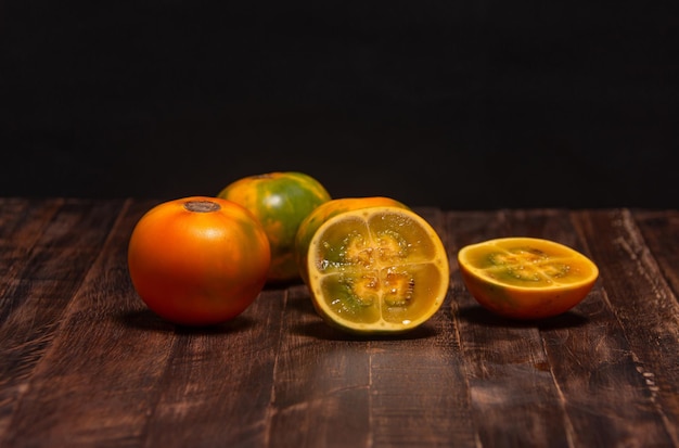 Lulo orgánico o naranjilla fruta exótica sudamericana. Frutas en la mesa y fondo oscuro. Solanum quitoense, alimento oscuro