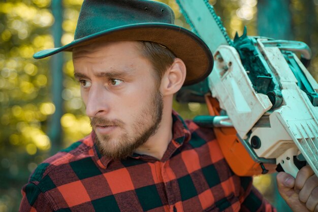 Lumberjack close up portrait Holzfäller mit Kettensäge in seinen Händen Holzfäller mit Axt oder Kettensäge im Sommerwald Holzfäller-Arbeiter zu Fuß im Wald mit Kettensäge