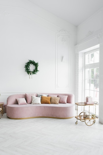 Luminoso y acogedor salón con un sofá rosa sobre el que cuelga una corona navideña cerca de la ventana francesa