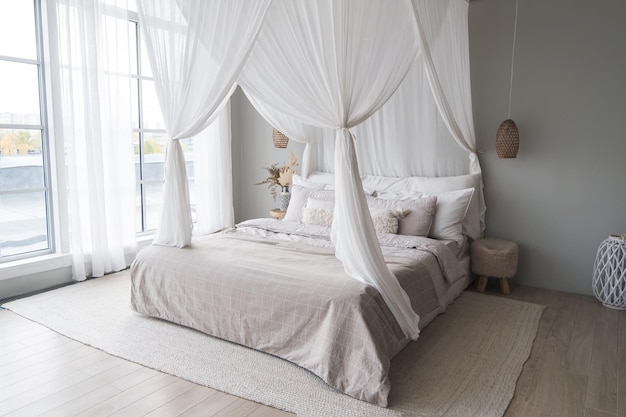 Luminoso interior de estilo escandinavo en el dormitorio Un dosel Una cama de lino y una alfombra de yute Ventanas de altura completa