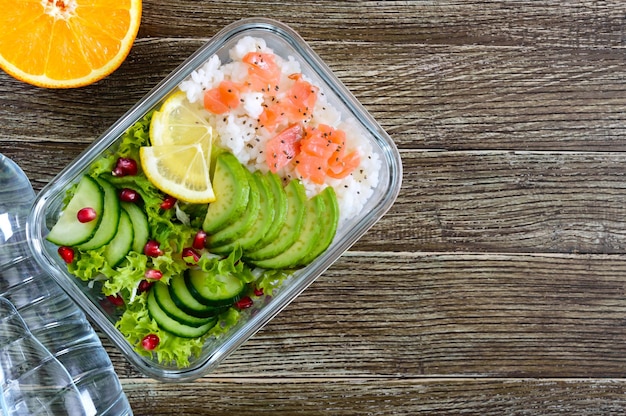 Lunch box arroz ensalada de salmón con pepino, aguacate, hojas de limón, semillas de chía y agua.