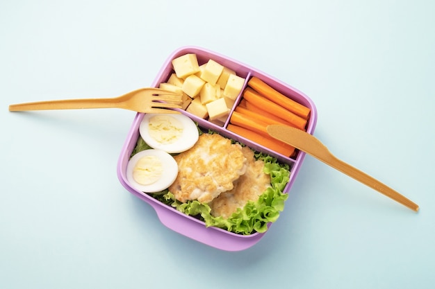 Foto lunchbox aus kunststoff mit gabel und messer auf blauem hintergrund