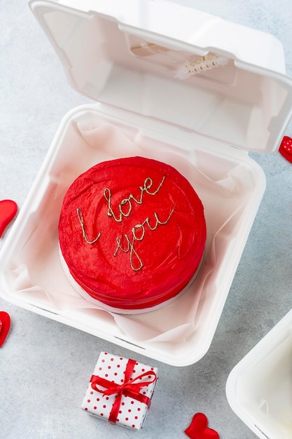 Lunchbox aus Kunststoff mit leckerem Bento-Kuchen und Geschenken zum Valentinstag auf weißem Hintergrund