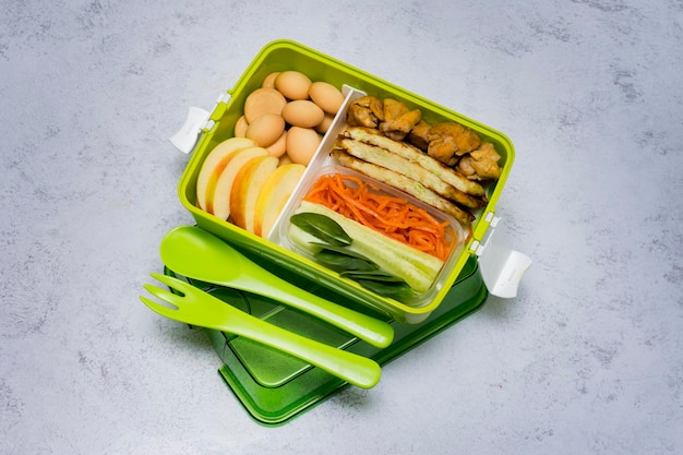 Lunchbox in grün mit Besteck Snack mit Hühnergurken Karotten Spinatblätter Apfel und Kekse zum Nachtisch in Scheiben schneiden Gesunde Ernährung KopierbereichDraufsicht