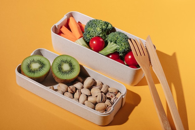 Lunchbox mit frischem Gemüse, Obst und Nüssen auf gelbem Hintergrund