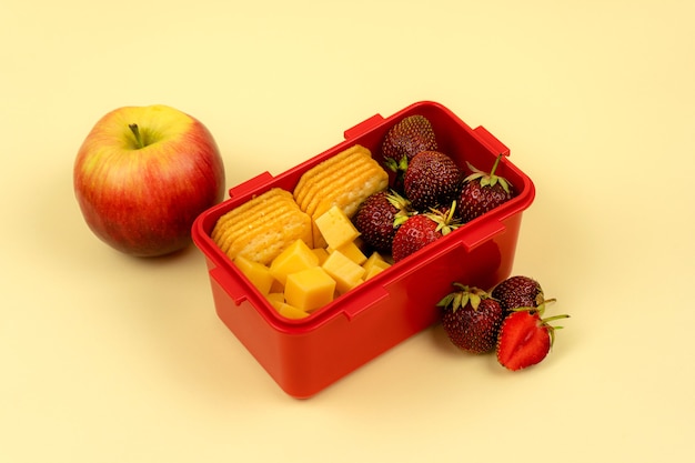 Lunchbox mit Früchten, Keksen und Käse für ein schnelles Mittagessen auf farbigem Hintergrund. Gesundes Essen.