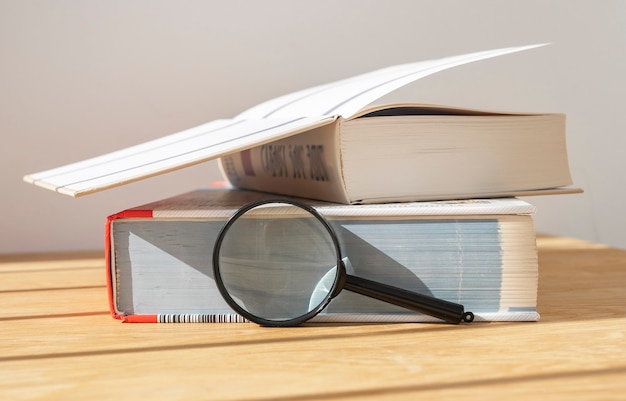 Lupa cerca de la pila de libros gruesos abiertos y cerrados en un escritorio de madera con luz natural